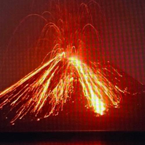 A volcano erupts spewing ash into the air and sending lava flowing down the side of the mountain. L