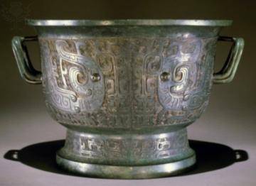 *An image of a bronze vessel is shown. The object has two handles on each side. It appears to have