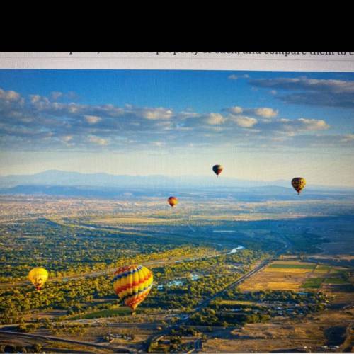 The picture shows several hot-air balloons floating near a river at the Albuquerque International B